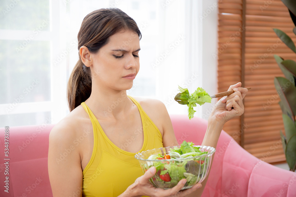 Young caucasian woman sitting on sofa eating vegetable salad while feeling dislike and expression disgusted, woman emotion frustrated with anorexia vegetarian and hate, nutrition food concept.