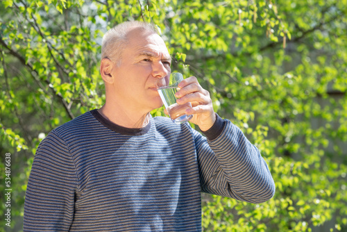 Thoughtful elderly man drinks water from a glass in nature photo