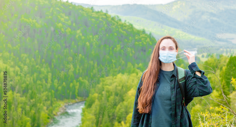 Young woman take off face mask after coronavirus and flu outbreak stands in mountains