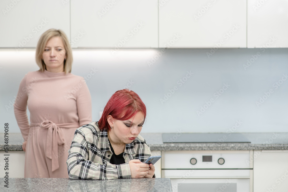 Unhappy mother looks at her teenage daughter, girl uses smartphone and ignores her mom. Family relationships. Empty space for text Unhappy mother looks at her teenage daughter, girl uses smartphone and ignores her mom. Family relationships. Empty space for text