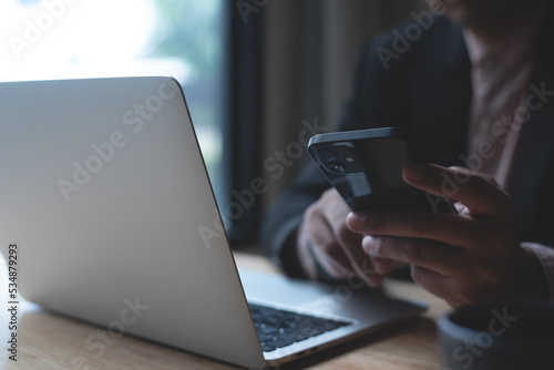 Businessman using mobile smart phone texting to colleague during working on laptop computer at office. Man manager sitting at table surfing the internet