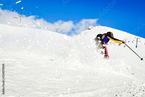 Dynamic picture of a skier on the piste in Alps. Woman skier in the soft snow. Active winter holidays, skiing downhill in sunny day.Ski rides on the track with swirls of fresh snow
