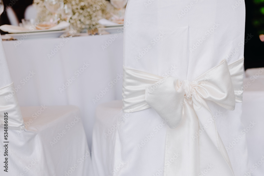 Chair cover with white ribbon tied with a bow at a wedding Chair cover with white ribbon tied with a bow at a wedding