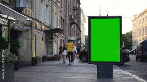 4k Billboard green screen stands and people walk along city street spbd. Mockup poster with advertising standing in open air, pedestrians walking and cars driving along road on summer day. Empty
