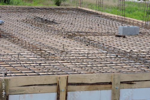 A steel reinforcement for the concrete floor and pillars on the first floor of a house under construction, a wooden formwork, a smoke and ventilation chimney, walls made of aac photo