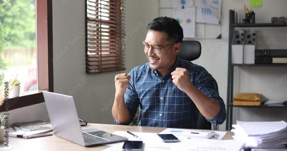 happy asian businessman and showing winner gesture while sitting at workplace in office. happy asian businessman and showing winner gesture while sitting at workplace in office.