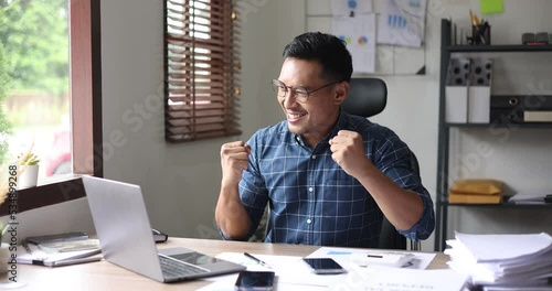 happy asian businessman and showing winner gesture while sitting at workplace in office.