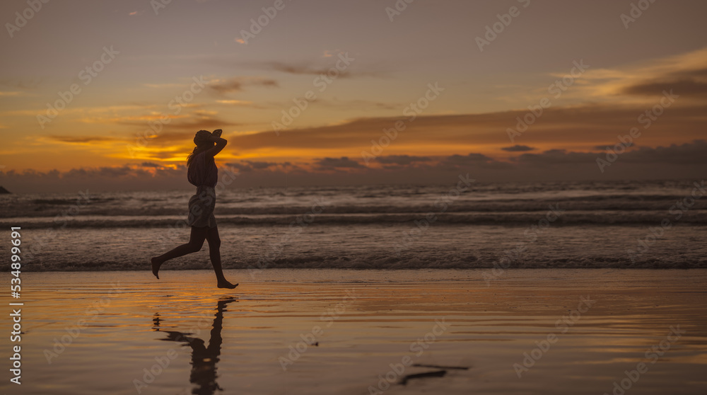 Silhouette of young Asian woman relaxing on a sandy beach at sunset