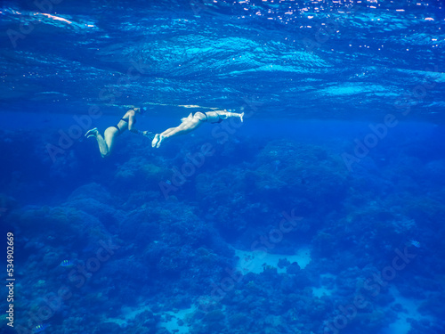 two young girls in black bikini swimming and snorkeling in clear blue sea water