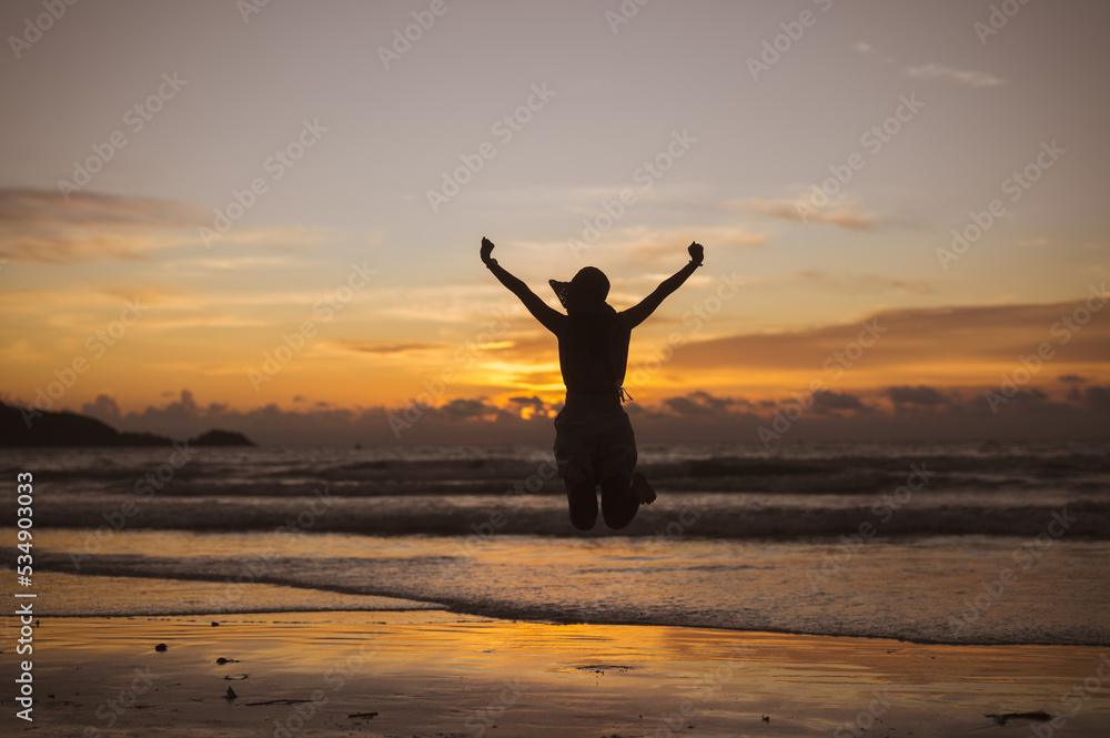 Silhouette of happy joyful woman jumping at the beach against the sunset. Freedom life vacation concept
