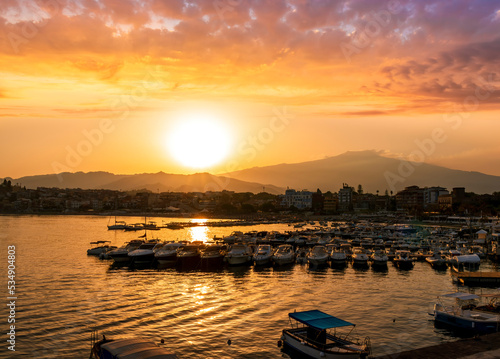 picturesque sunrise or sunset in a sea port with a gulf dock pier with tour boats and a town with cloudy sky on background of a seashore landscape © Yaroslav