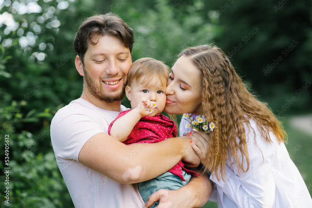 Fototapeta premium Happy young beautiful family with a young son is enjoying a wonderful day in a summer park. Young parents kiss a child