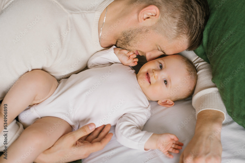 A handsome young dad lies in bed in the bedroom and hugs his loving laughing six-month-old boy. The concept of unconditional love and fatherhood A handsome young dad lies in bed in the bedroom and hugs his loving laughing six-month-old boy. The concept of unconditional love and fatherhood