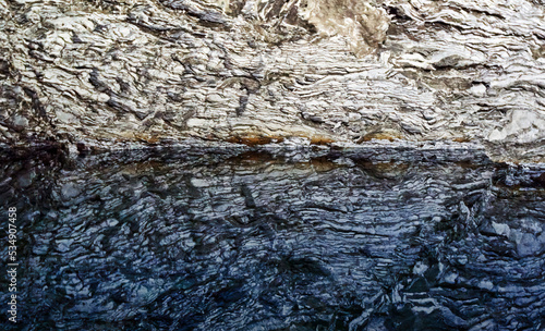 Reflection of anhydrite banded by clay deposits in the water of a subterranean groundwater lake in a cave photo
