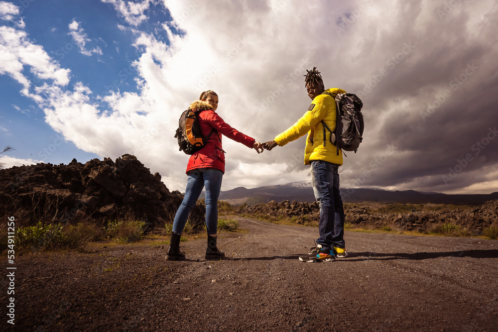 Multiethnic couple of hiker lovers holding hands and looking at the camera through the lava stone
