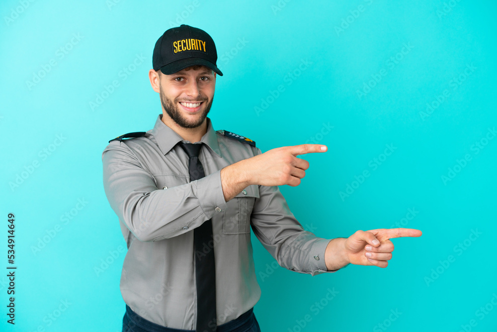 Young security man isolated on blue background pointing finger to the side and presenting a product Young security man isolated on blue background pointing finger to the side and presenting a product