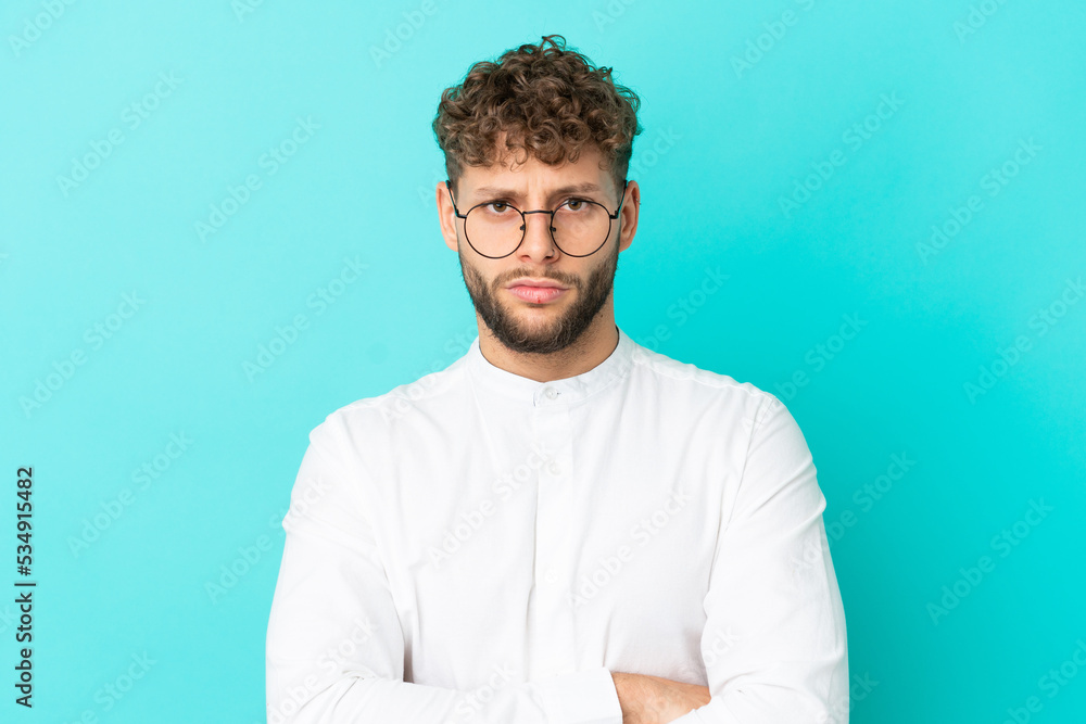 Young handsome caucasian man isolated on blue background With glasses and arms crossed Young handsome caucasian man isolated on blue background With glasses and arms crossed