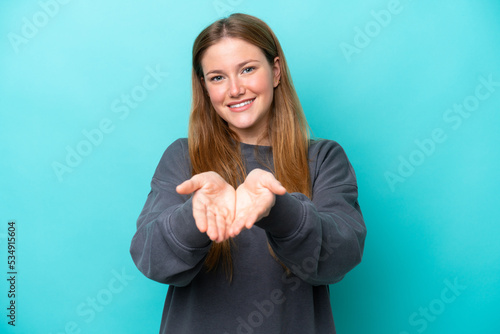 Young caucasian woman isolated on blue background holding copyspace imaginary on the palm to insert an ad