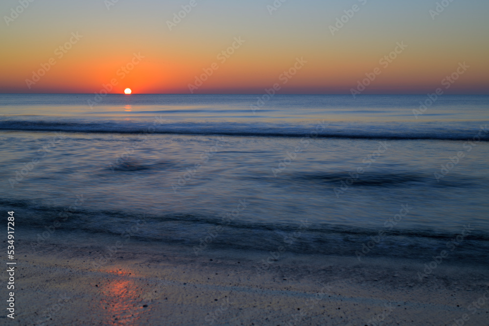 Sonnenuntergang über dem blauem Meer und sanfte Wellen spülen an den Strand.