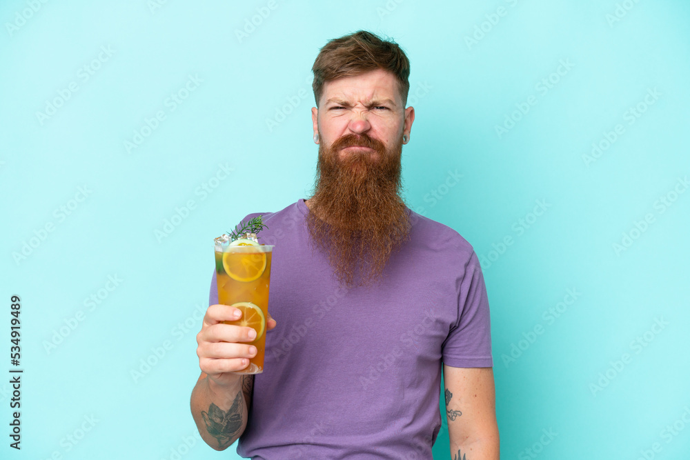 Redhead man with long beard holding a cocktail isolated on blue background with sad expression Redhead man with long beard holding a cocktail isolated on blue background with sad expression