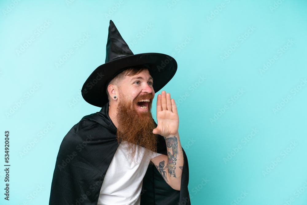 Naklejka premium Young wizard in halloween isolated on blue background shouting with mouth wide open to the side