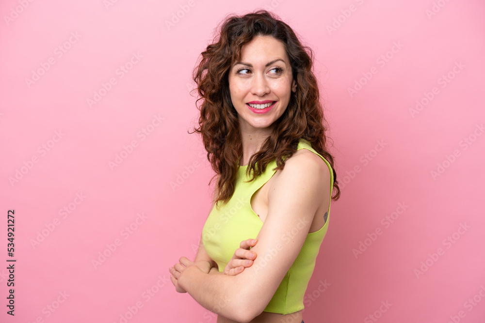 Young caucasian woman isolated on pink background with arms crossed and happy