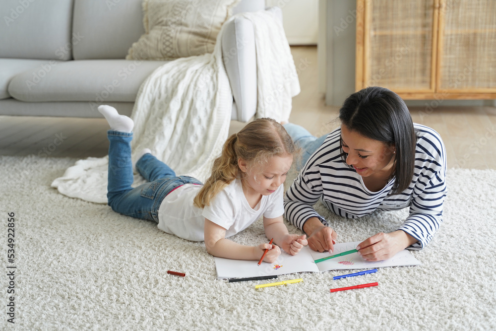 Kid girl daughter and mom drawing painting lying on floor carpet together. Children's education