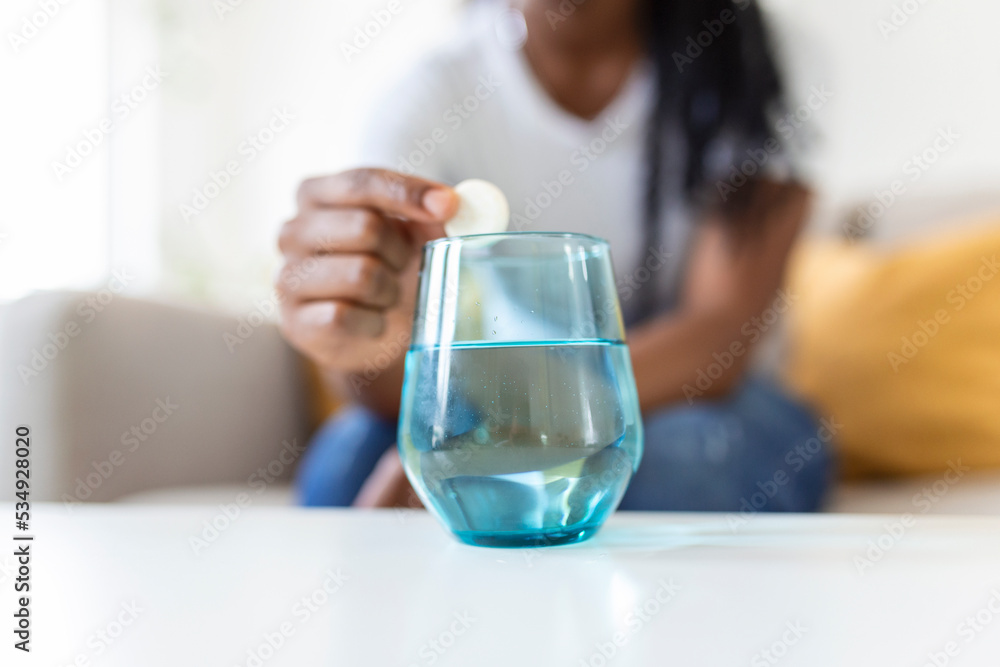Closeup of a young woman dropping an effervescent antacid in a glass of water. young woman hardly put a soluble pill with a medicine for pain or a hangover in a glass of water Closeup of a young woman dropping an effervescent antacid in a glass of water. young woman hardly put a soluble pill with a medicine for pain or a hangover in a glass of water
