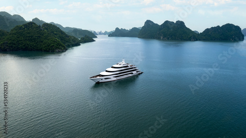 beautiful white luxury mega yacht in tropical Ha Long Bay Vietnam with large limestone mountains, aerial