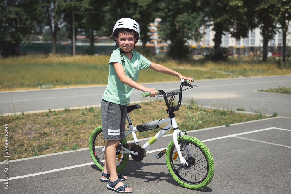 Charming active Caucasian child boy, in protective helmet, looking at camera, standing near his bicycle on the asphalt road outdoor. Physical activity. Active lifestyle. Equilibre and balance. Sport Charming active Caucasian child boy, in protective helmet, looking at camera, standing near his bicycle on the asphalt road outdoor. Physical activity. Active lifestyle. Equilibre and balance. Sport
