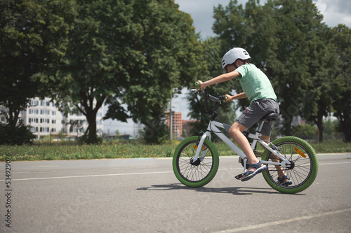 A school-age boy learns extreme tricks and extreme cycling in the city. Sporty child in protective gear riding a bicycle  cycling on the asphalt road outdoors. Sport. Active  healthy lifestyle concept