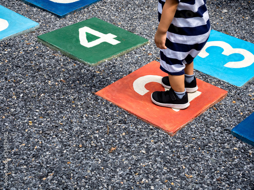 A little young boy standing on number 2 on multicolored hopscotch on the asphalt ground in the kids playground, outdoors game activities for children. Growth and moving forward concept. photo