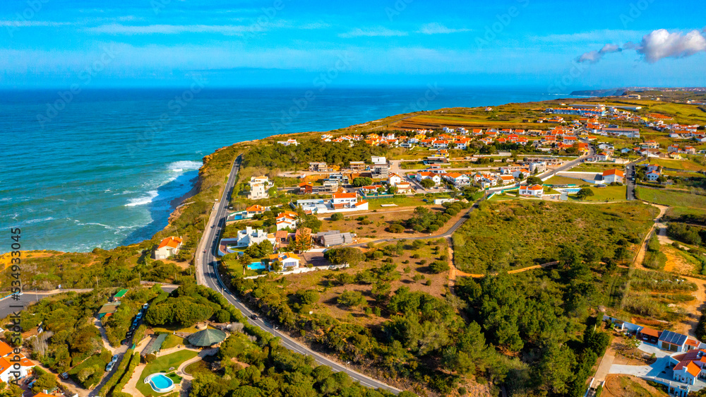 Aerial view of a small European town against blue sky and Atlantic Ocean. Drone view of a beautiful European city with a hilly landscape on ocean background. Beautiful natural landscape. Portugal.