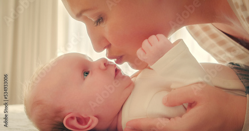 Adult Mother kissing her newborn son. Closeup portrait of a loving mother's kiss. Young mom kissing beautiful infant baby. Mum loves of her infant baby. Parenthood concept.