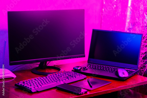Workplace of a graphic designer and creative retoucher. Graphic tablet, smartphone and computer equipment in neon light. Workspace of creative designer with tablet and stylus