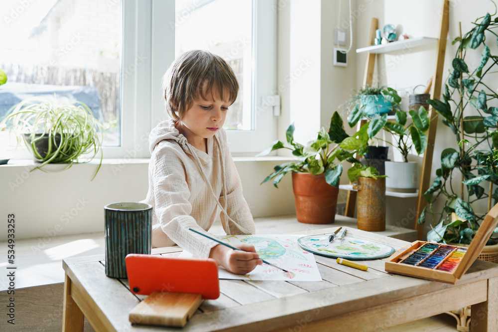 Preschooler boy paining by multicolored paints with online lesson on smartphon Preschooler boy paining by multicolored paints with online lesson on smartphon