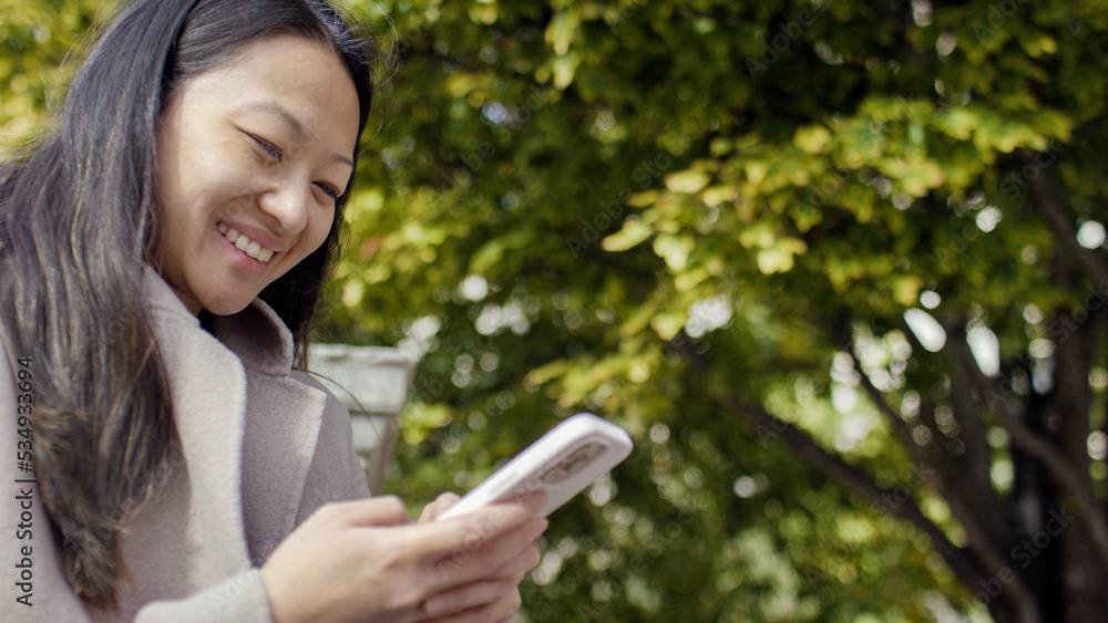Young woman smiles at her phone outdoors in a park, with space for text