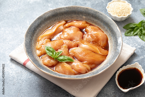 Raw diet marinated chicken meat with teriyaki sauce in a grey bowl. Marinating meat for cooking barbecue