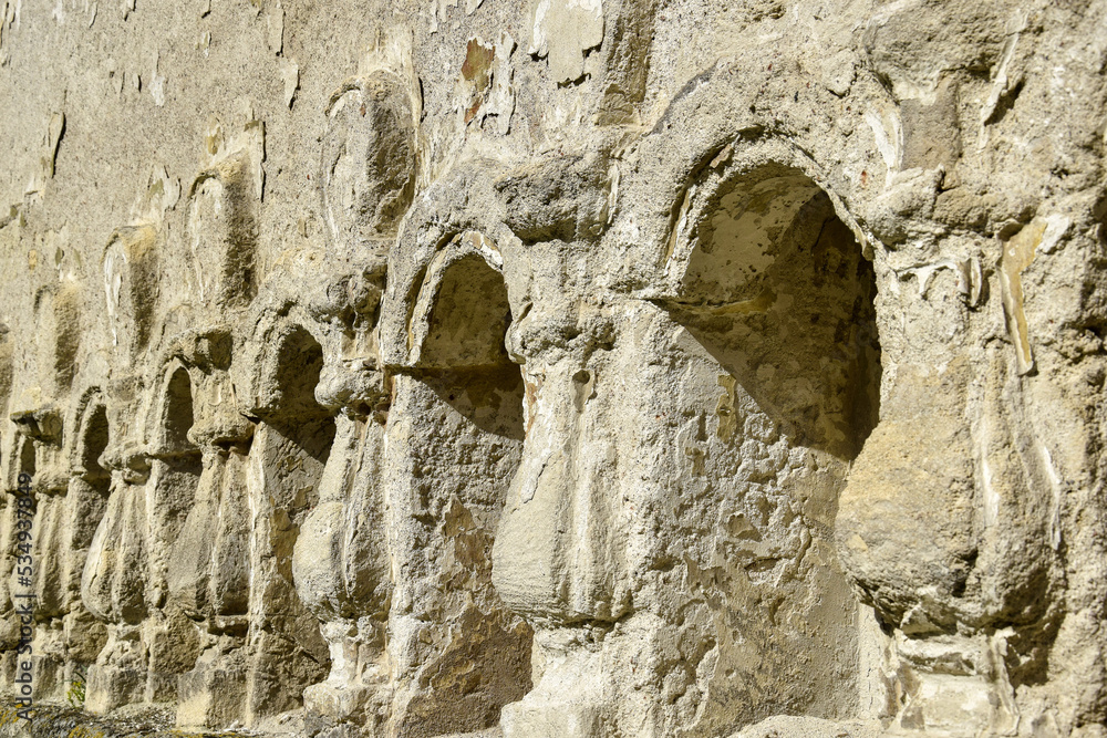 Stone relief columns carved in the wall. Texture of old dilapidated masonry. Ancient half-ruined synagogue. Rashkov, Moldova. Selective focus.