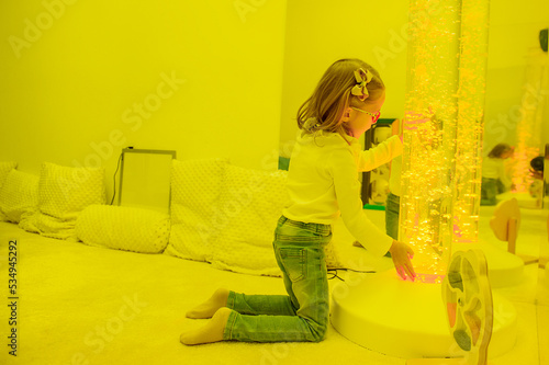 Child in sensory room, snoezelen, interacting with colored lights bubble tube lamp during therapy session. Child with cerebral palsy in occupational therapy. photo