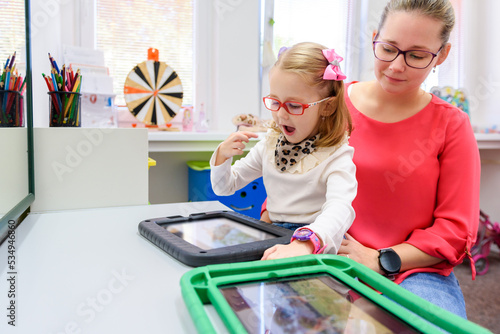 Non-verbal girl living with cerebral palsy, learning to use digital tablet device to communicate. People who have difficulty developing language or using speech use speech-generating devices. photo