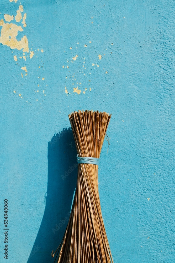 Coconut broom stick isolated in blue color painted wall background. Traditional cleaning broom