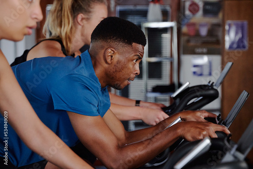 Group of focused young multiracial adults doing cardio on exercise bike at the gym