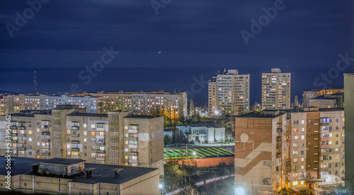 The roofs and windows of the houses and the stadium between the houses glow at night under the blue starry sky