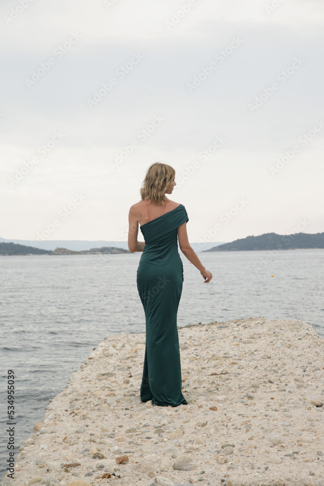 Fashion outdoor portrait of female model in long elegant green dress on the beach