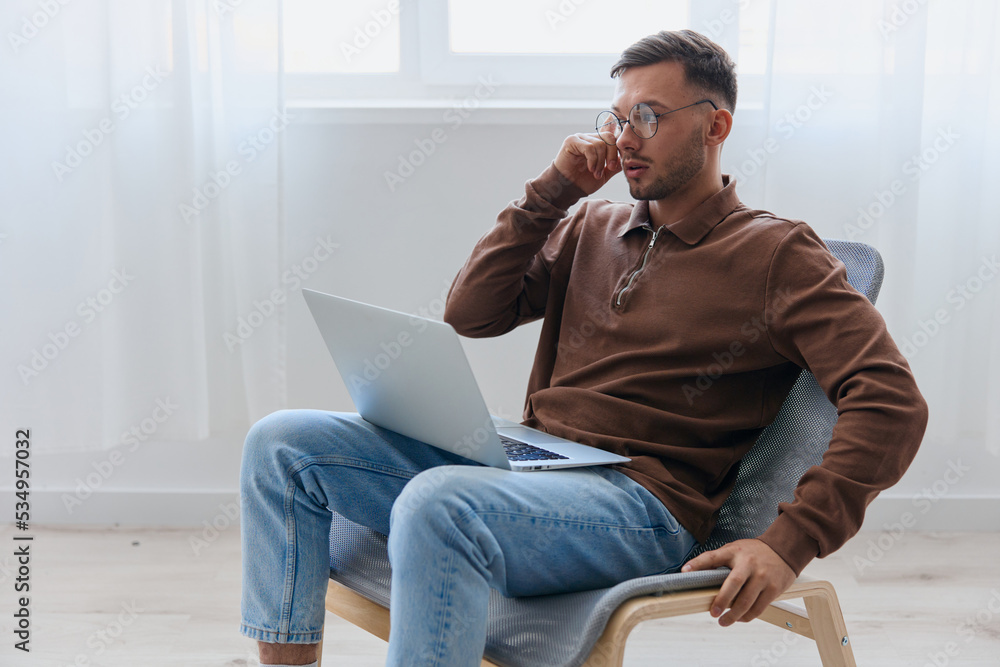 Modern Profession offer. Pensive young man in eyewear typing report for work project think about right decision for work screen sitting in chair at home. Remote Job Distant Work Communication concept