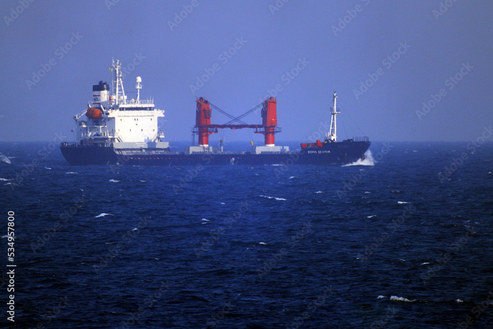 A large ship at full speed floats splashing water on the blue sea among the waves