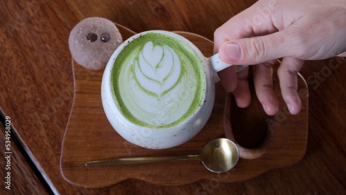 Top down view of a beautifully served cup of matte green tea with an ingenious pattern on the milk froth. The cup stands on a wooden tray in the same color scheme as the table.