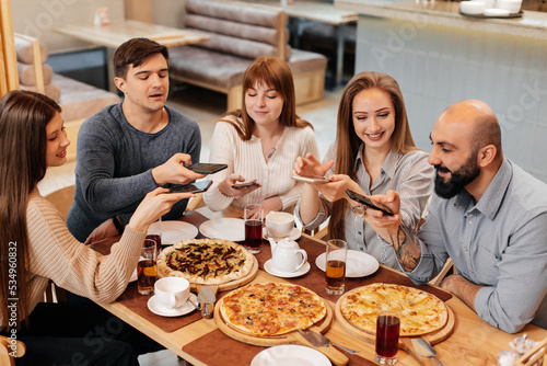 A group of friends is having pizza in a cozy restaurant and taking selfies, taking pictures together. A cheerful group of friends.