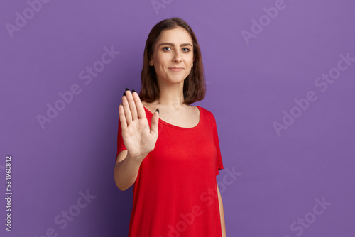 Dont worry I will do it myself. Happy young pretty brunette girl show stop gesture and smiling. Looking at the camera with confidence. Wearing a red t-shirt and posing over purple background.